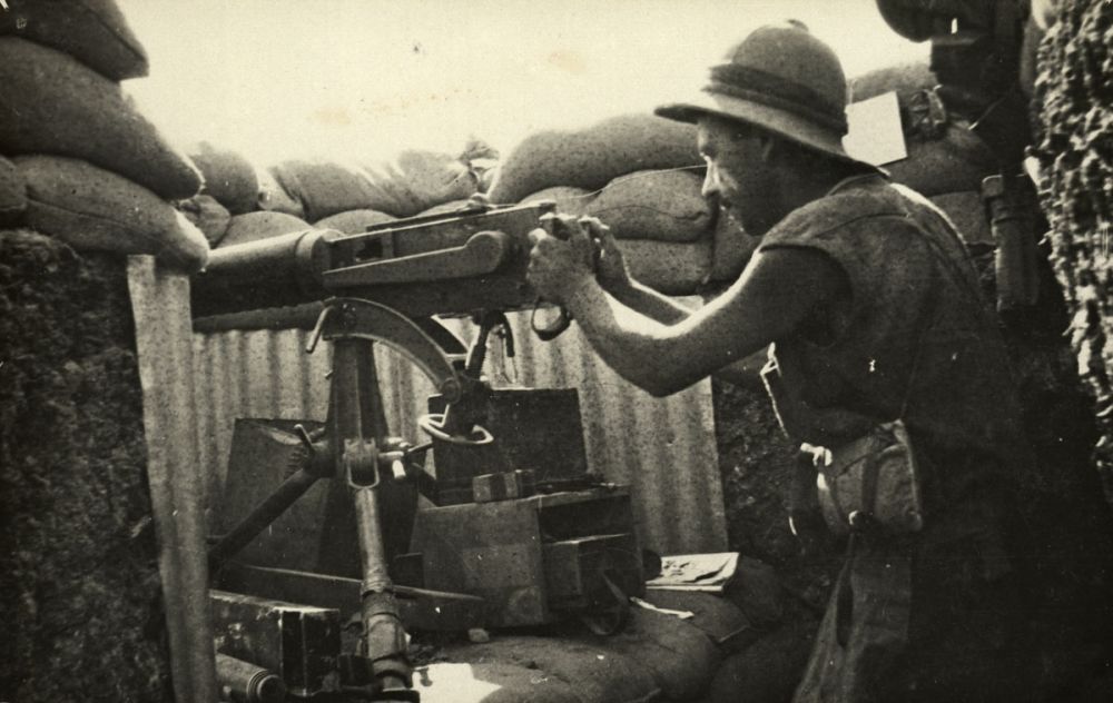 Robert Cardno poses with a machine gun. There is a periscope to the left of the gun.